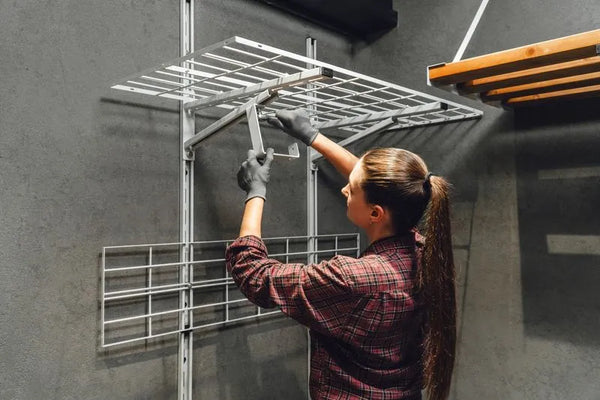 Person installing metal shelving units on a gray wall.