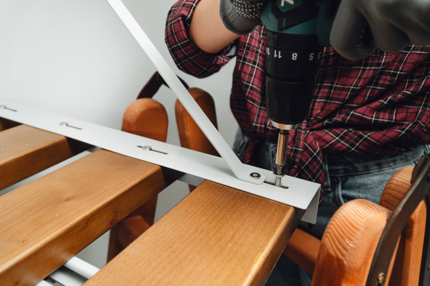 Person using a drill on a wooden surface with a white bracket
