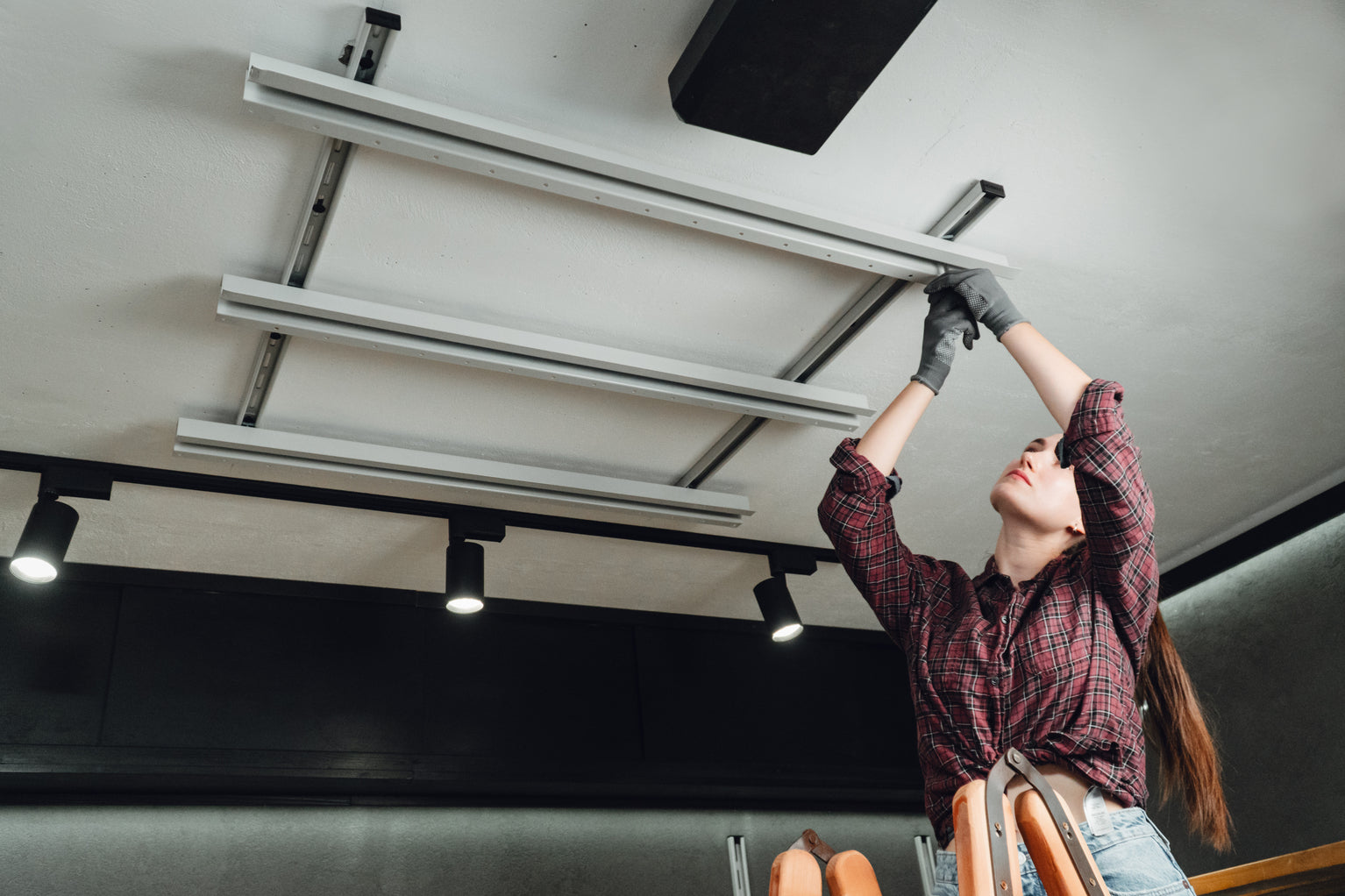 Person installing a ceiling-mounted ladder in a room with lights and a white ceiling.