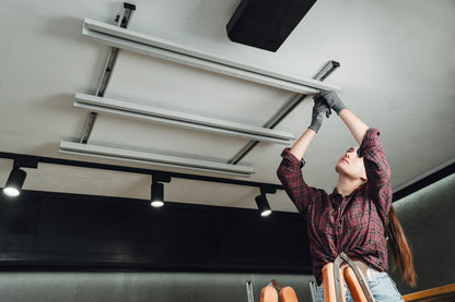 Person installing a ceiling-mounted ladder in a room with lights and a white ceiling.
