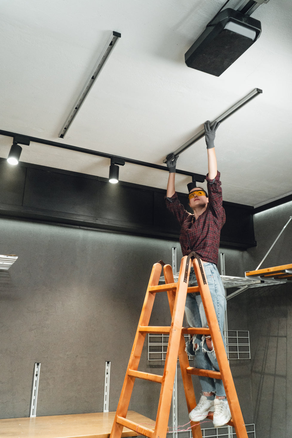 Person on a ladder installing or adjusting ceiling lights in a modern indoor setting.