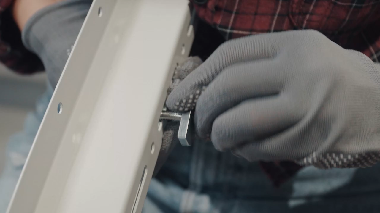 Person wearing gloves using a tool on a metal frame