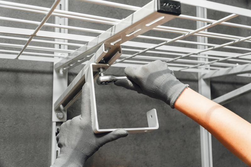 Using a power driver with a socket attachment to secure a metal Ezyrack wall channel to a white wall with a hex bolt.
