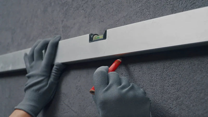 Image showing the second step of installation, demonstrating the use of a power drill to secure a heavy-duty steel bracket to the marked wall.