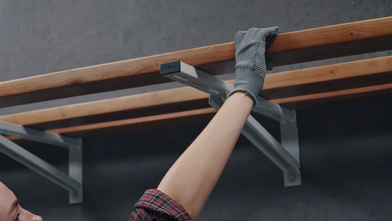 Installing wooden planks on metal shelving brackets against a dark grey wall.