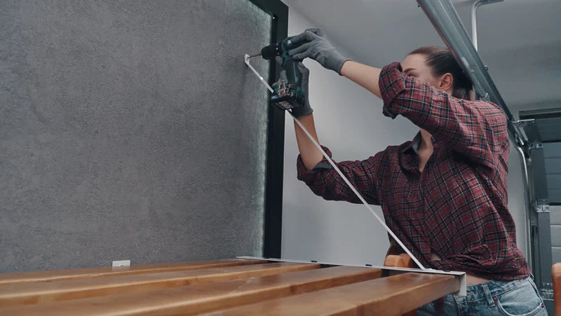Image showing the installation of timber straps, featuring a person using a power drill to secure a support strap from the wall to a wooden shelf.